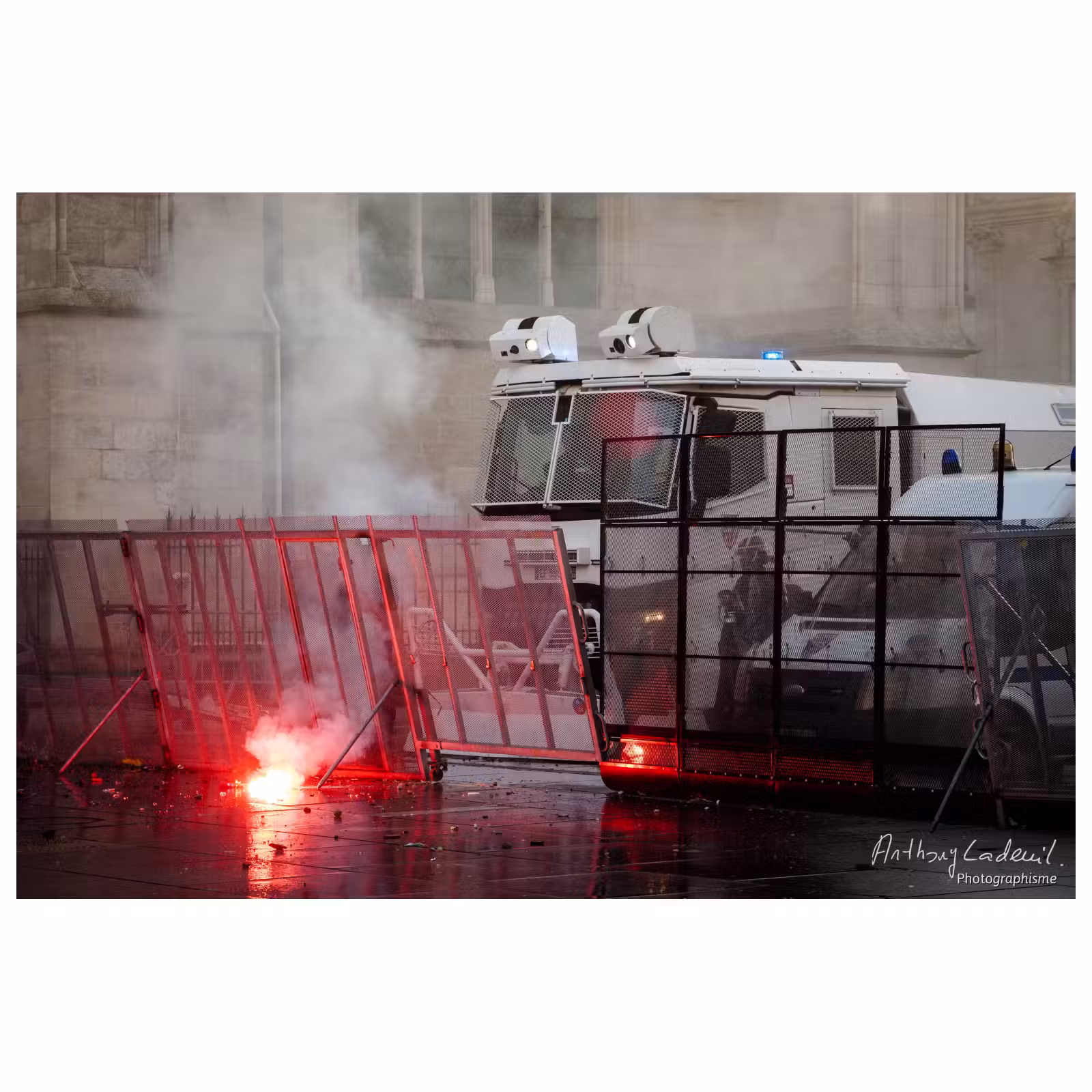 un fumigène incandescent brûle devant des CRS à l'arrière d'une barricade