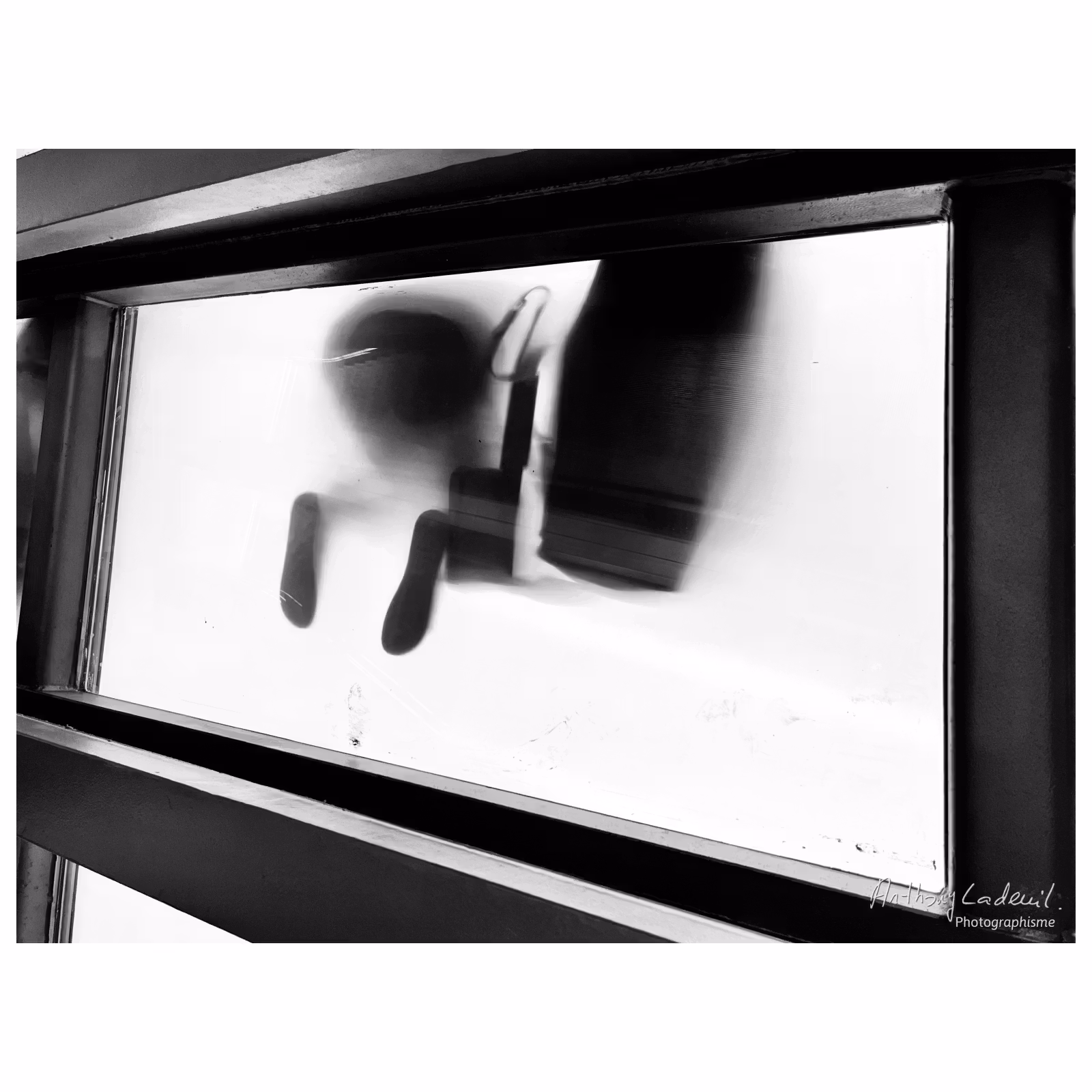 photographie en noir et blanc en contre-plongée sous une passerelle semie transparente où on voit des pieds en contre jour