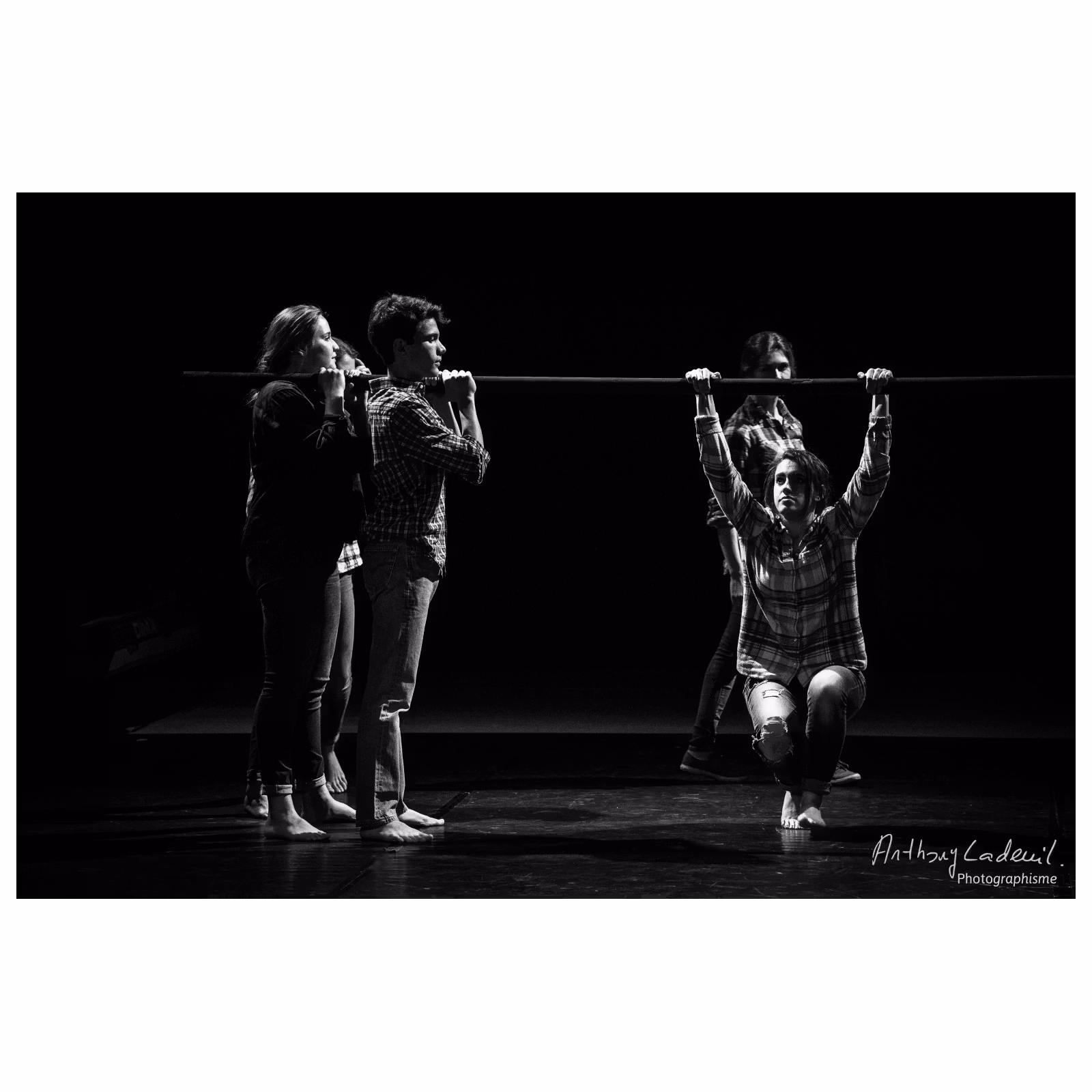 jeunes artistes de cirque tenant une barre sur laquelle est suspendu un garçon