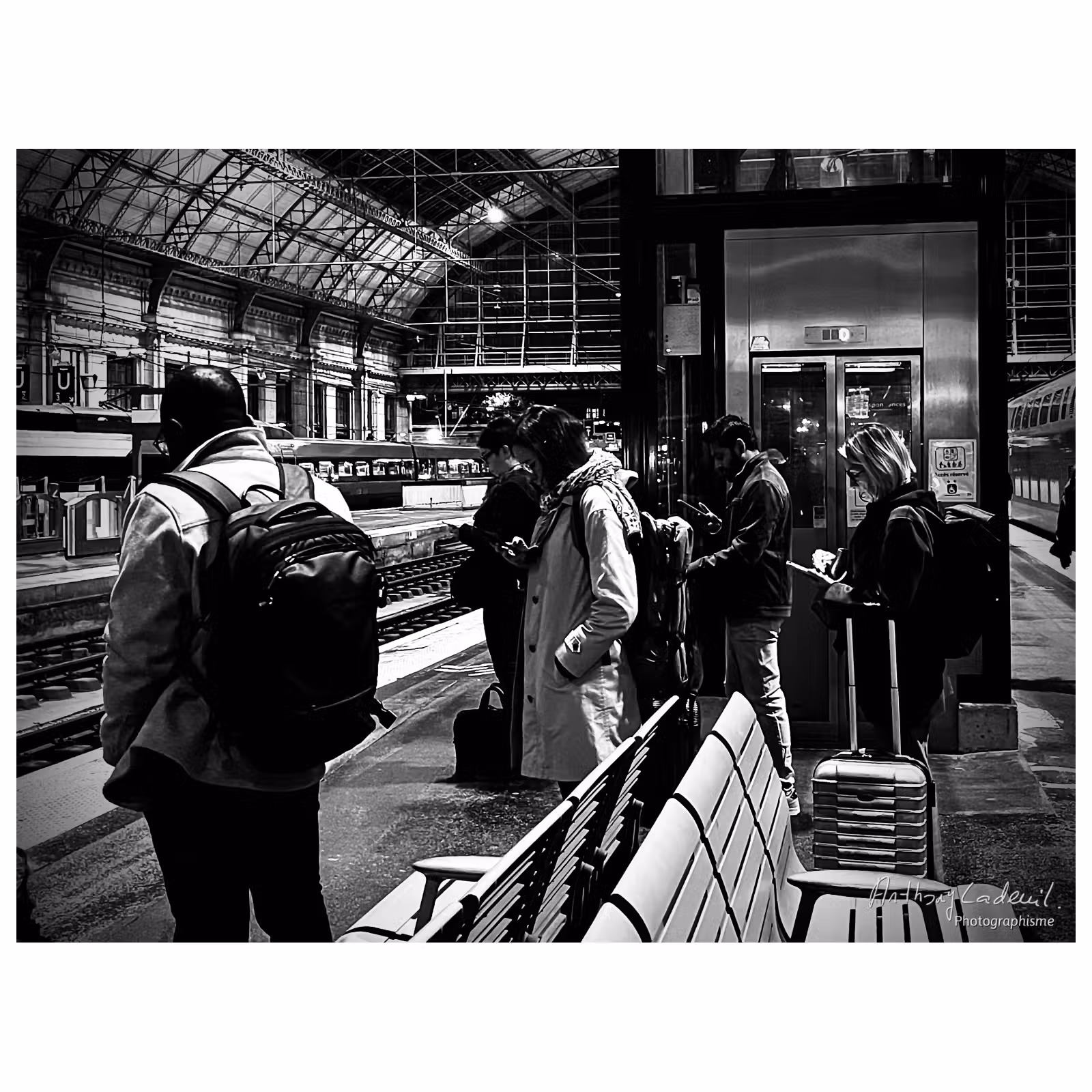 des personnes sur un quai de gar, toutes en train de regarder leurs téléphones la tête baissée