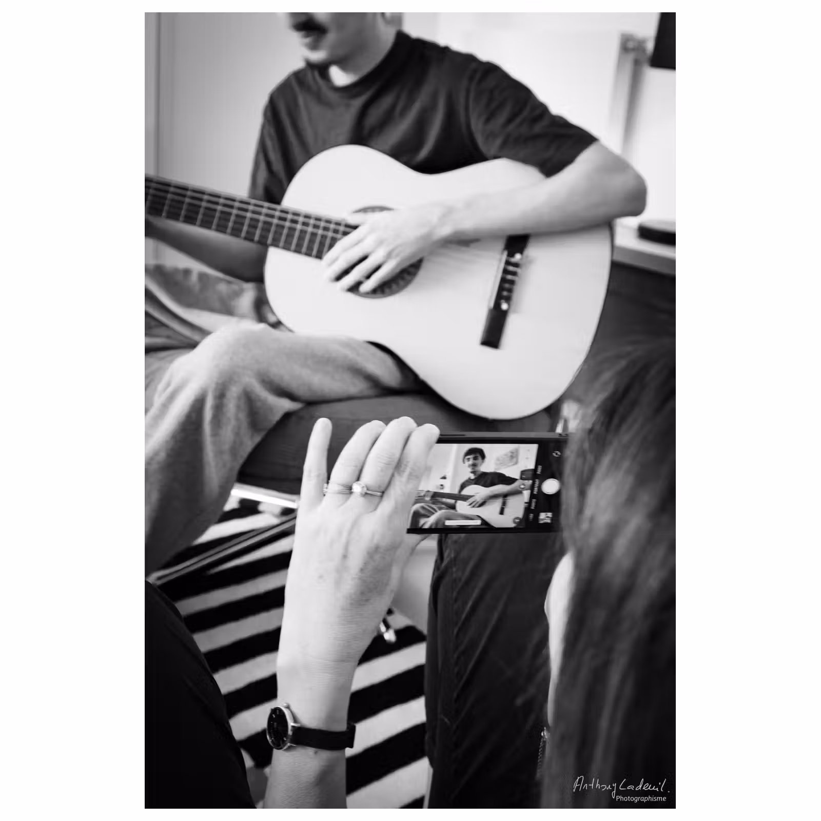 un jeune homme joue de la guitare en arrière plan d'un téléphone portable qui le prend en photo