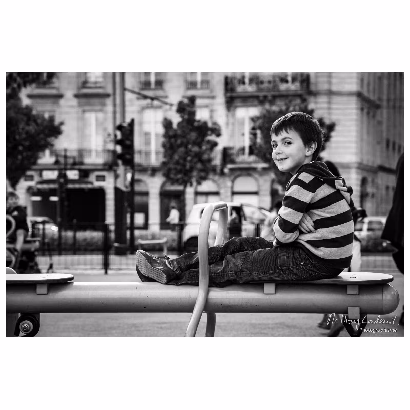 Photographie de rue sur les quais de Bordeaux. Un enfant sourit, assis sur un jeu de plein air.