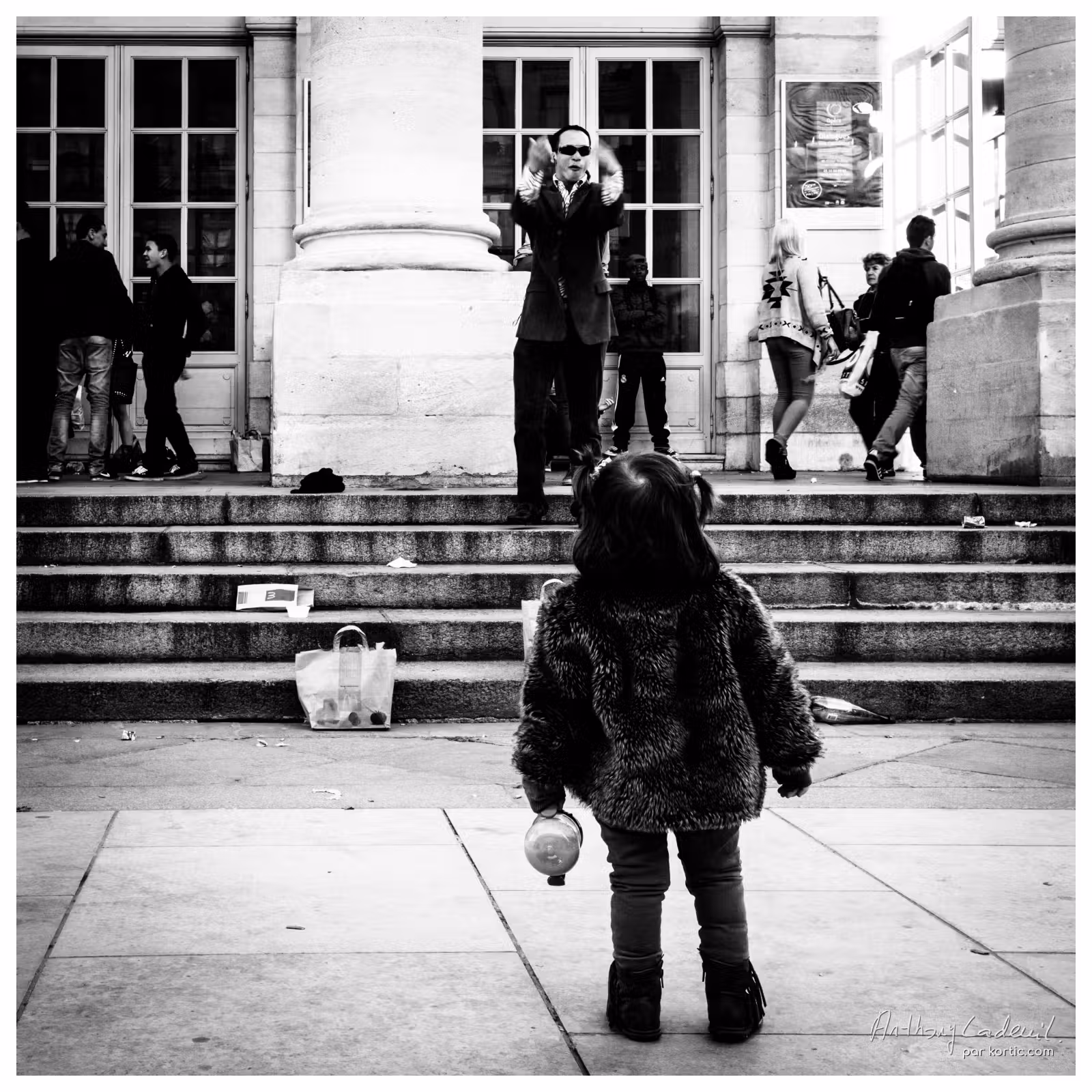 jeune enfant vue de dos en train de regarder un homme qui chante dans la rue