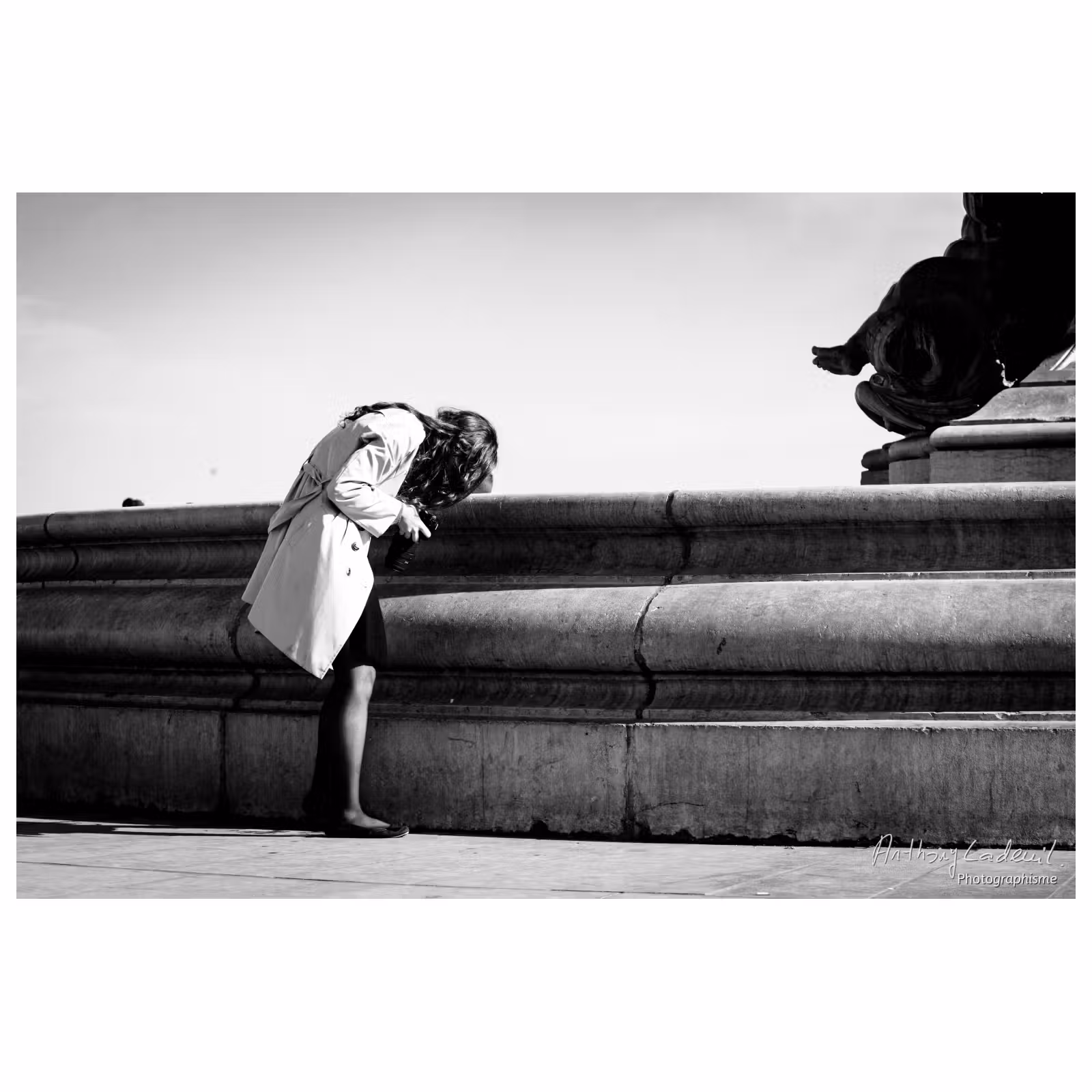 jeune femme courbée qui regarde l'écran de son appareil photo dans la rue devant une fontaine