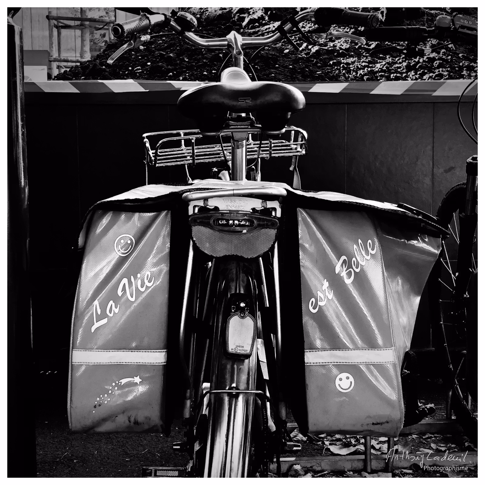 photographie en noir et blanc de l'arrière d'un vélo avec des sacoches où est écrit « la vie est belle »