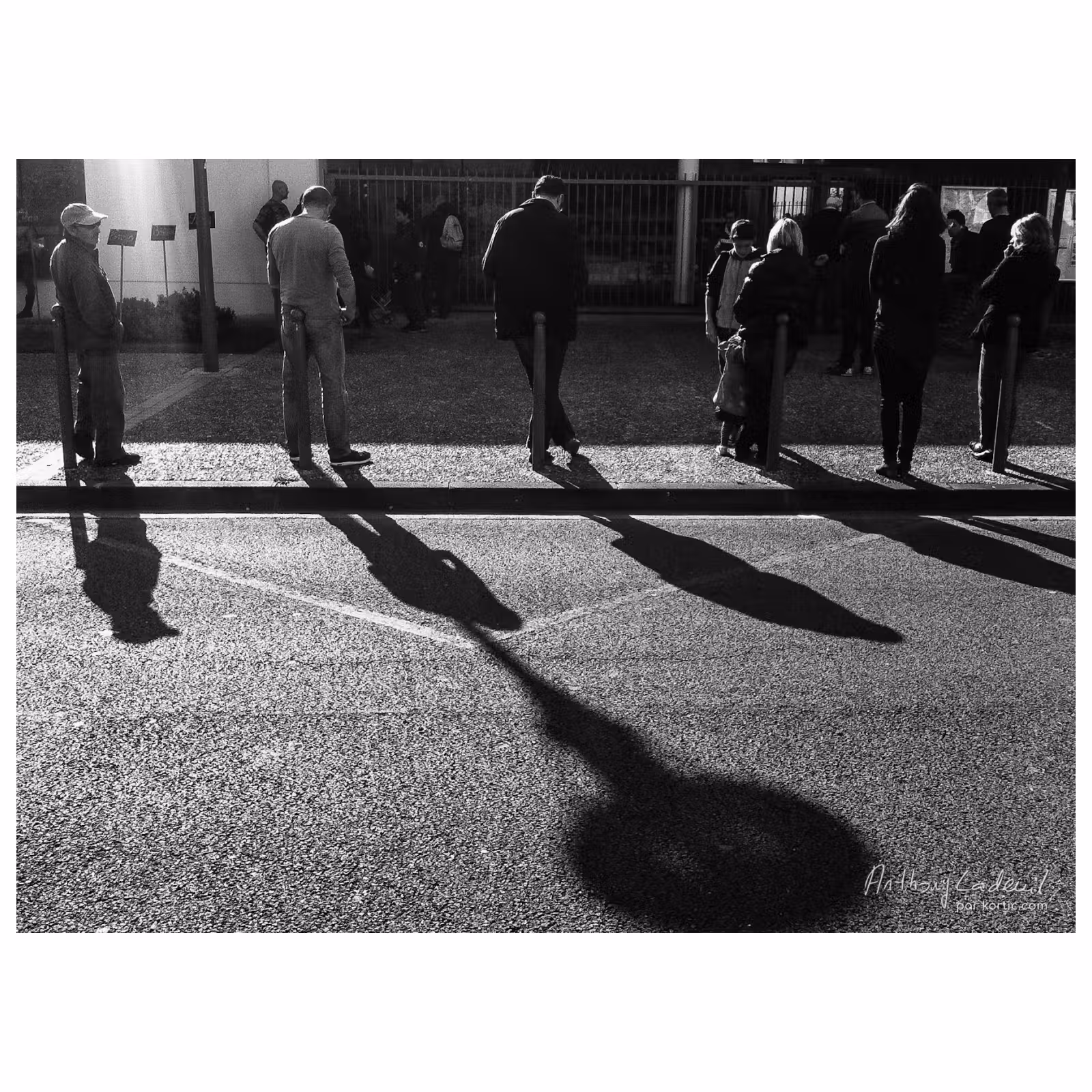 suite de personnes vues de dos appuyées sur des poteaux en bordure de trottoir