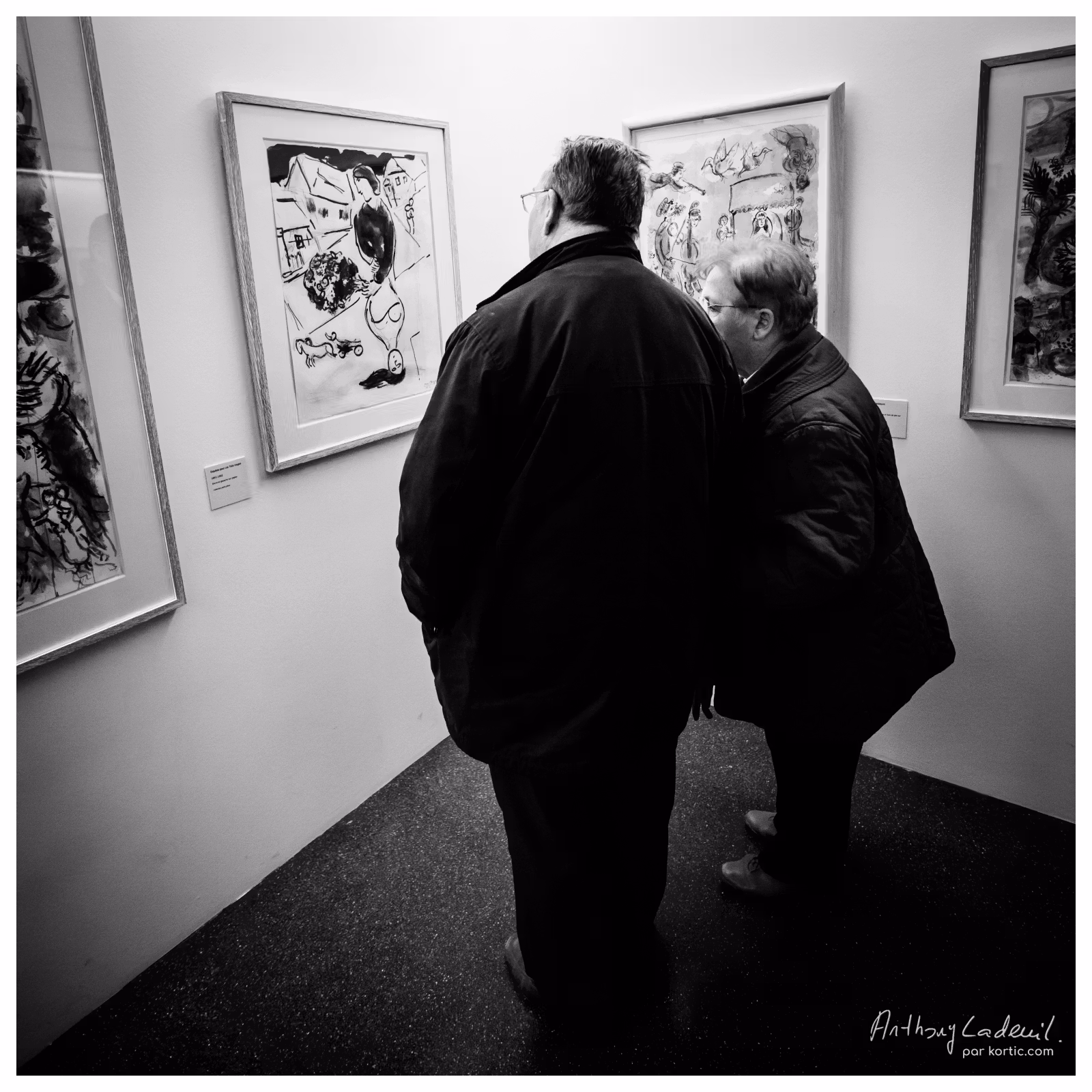 un homme et une femme vus de dos en train de regarder des tableaux exposés