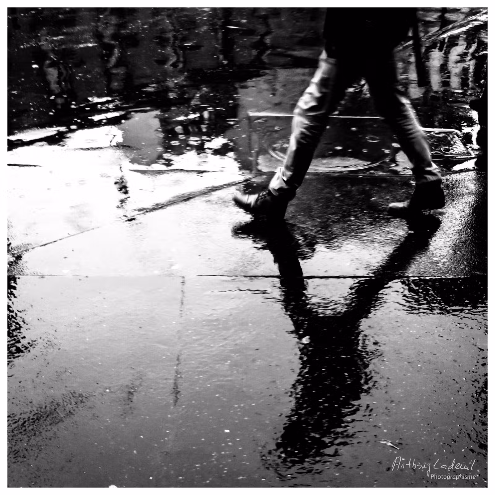 photo du sol d'une rue détrempée par la pluie avec le reflet d'un passant qui marche