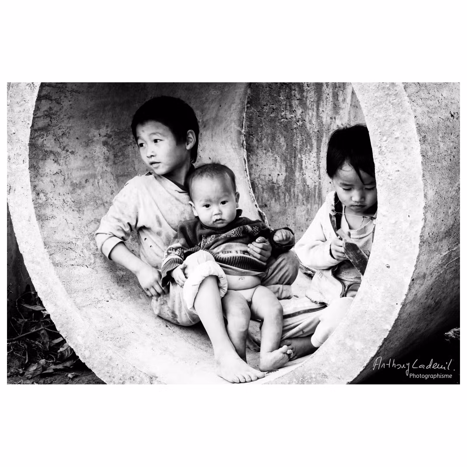 Trois enfants vietnamiens qui jouent dans un tube en béton