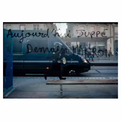 tags menaçants contre Emmanuel Macron sur les vitres d'un abri de bus avec un fourgon de CRS en arrière plan