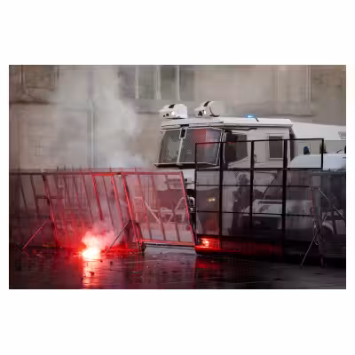 un fumigène incandescent brûle devant des CRS à l'arrière d'une barricade