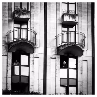 Photographie noir et blanc d'une façade d'immeuble avec deux personnes à leurs fenêtres