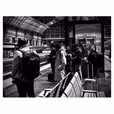 des personnes sur un quai de gar, toutes en train de regarder leurs téléphones la tête baissée