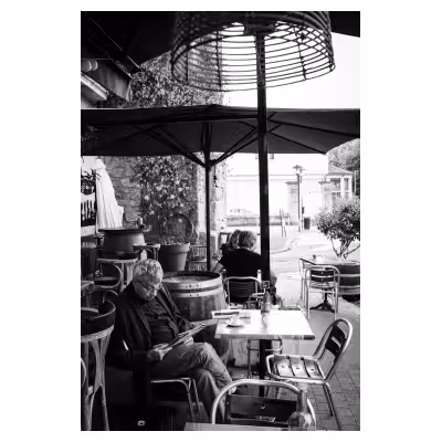 photographie d'un homme assis sur une terrasse de café lisant un journal
