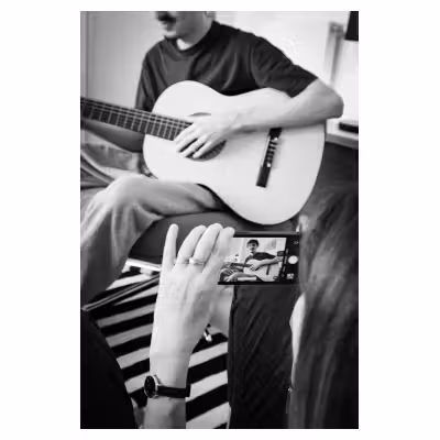 un jeune homme joue de la guitare en arrière plan d'un téléphone portable qui le prend en photo