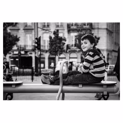 Photographie de rue sur les quais de Bordeaux. Un enfant sourit, assis sur un jeu de plein air.