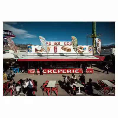 Stand de crêperie et bonbons dans une fête foraine avec des personnes attablées devant