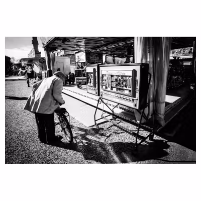 vieil homme et son vélo qui regarde une machine ancienne à tirettes dans une fête foraine