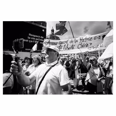 un homme prend une photo de lui même devant une banderole manuscrite dans une manifestation