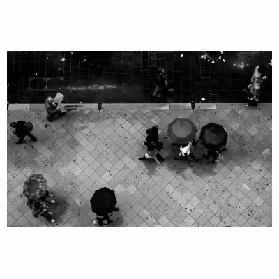 Photographie en plongée d'une rue ou des personnes marchent en file avec des parapluies