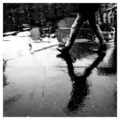 photo du sol d'une rue détrempée par la pluie avec le reflet d'un passant qui marche