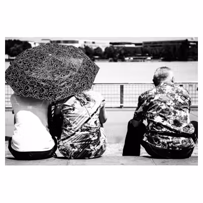3 personnes vues de dos assises avec des chemises bariolées et un parapluie