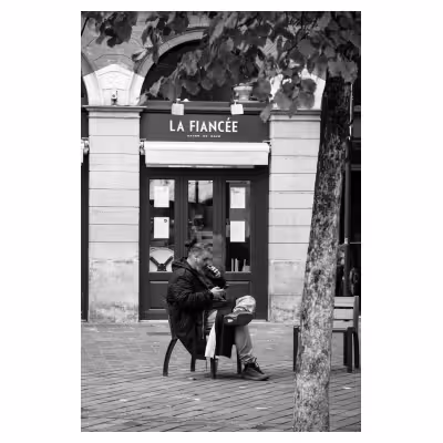 photographie d'un homme assis sur un banc devant un magasin nommé « la fiancée »