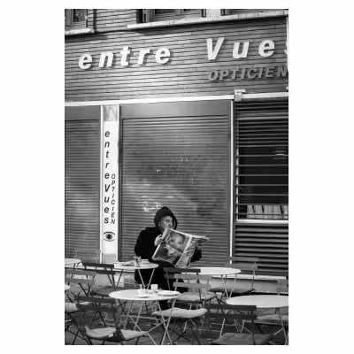 photographie d'un homme lisant le journal sur une terrasse devant un magasin d'optique